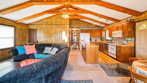 A spacious living area with a sofa, a kitchen with wooden cabinets, and a dining table. - Three Sheets to the Wind - Dog-friendly Lakefront Home With Dock, & Kayaks (Moneta)