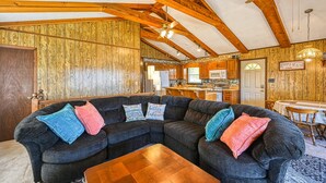 A cozy living room with a sectional sofa, wooden beams, and a kitchen in the background. - Three Sheets to the Wind - Dog-friendly Lakefront Home With Dock, & Kayaks (Moneta)