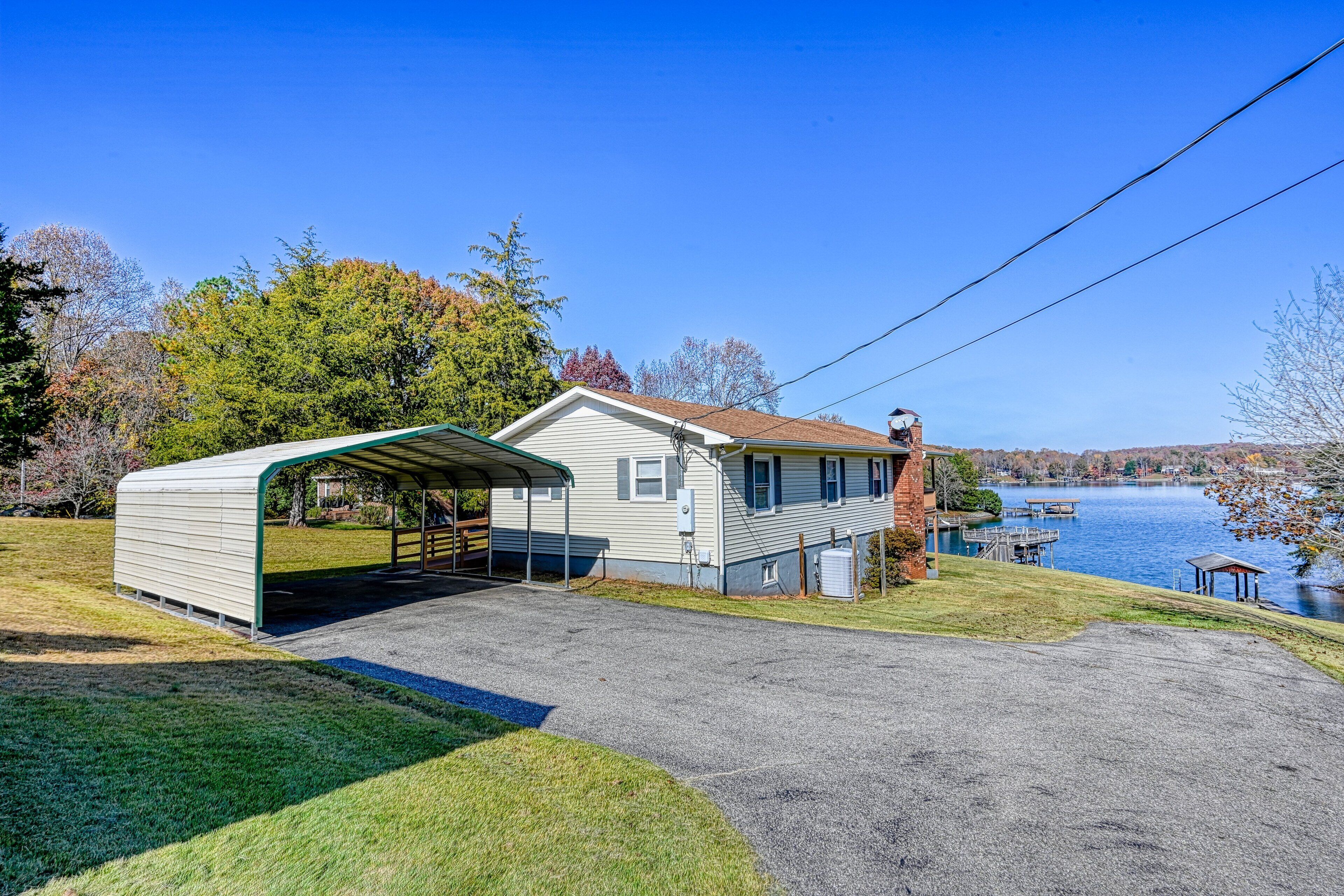 A house with a covered garage, a dock by the lake, and a clear sky.