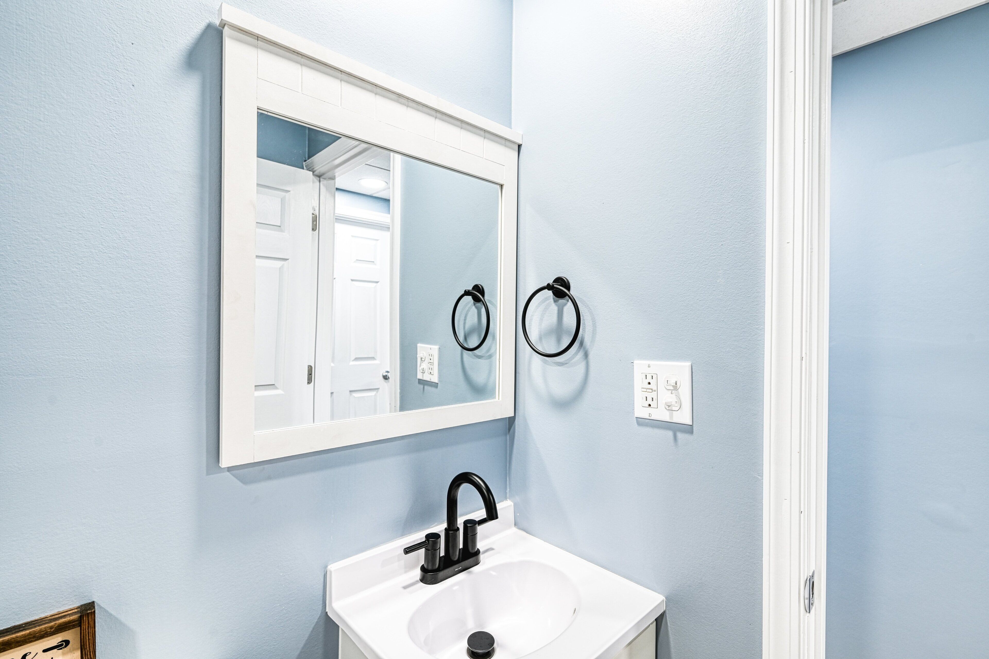 A bathroom with a white sink, a large mirror, and two towel rings on the wall.