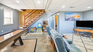 A living room with a pool table, a blue sofa, a TV, and a staircase. - Three Sheets to the Wind - Dog-friendly Lakefront Home With Dock, & Kayaks (Moneta)