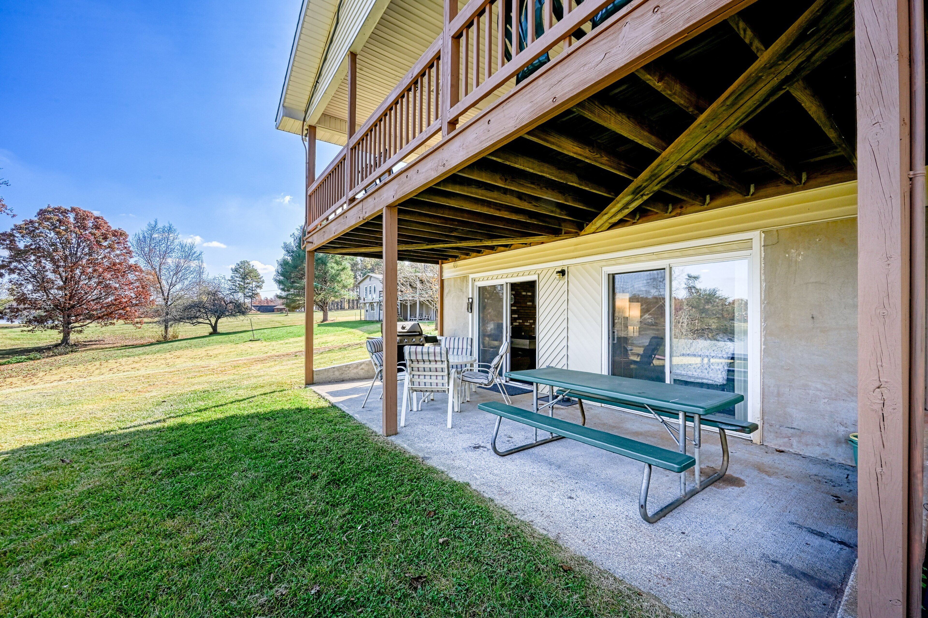 A covered patio with a picnic table and chairs, a grill, and a view of the surrounding landscape.