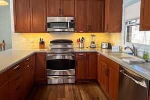A kitchen with wooden cabinets, stainless steel appliances, a toaster, and a window with blinds. - Lakedaze - Spacious Dog-friendly Lakefront House W/dock, hot tub & Putting Green (Moneta)