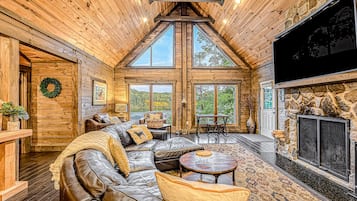 A log cabin interior with a leather sofa, stone fireplace, and large windows.