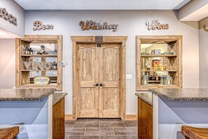 A bar area with wooden doors, shelves with liquor bottles, and a sign reading 'Deep Eddy Lemon.' - Cabin on the Cove - Luxe Lakefront Pet Friendly Cabin on 5 Acres With Huge Dock (Moneta)