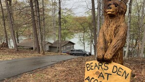 Una escultura de madera de un oso sosteniendo un letrero que dice 'BEARS DEN AT ACORN DR'.