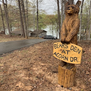 A wooden bear sculpture holding a sign that reads 'BEARS DEN AT ACORN DR.'
