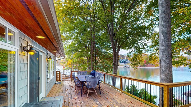 Una terraza de madera con mobiliario exterior, barandilla y vista a un lago.