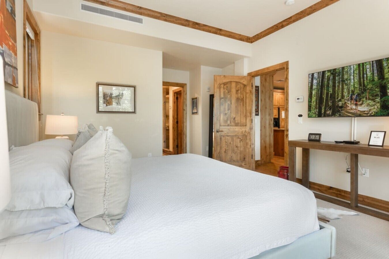 A bedroom with a large bed, a bedside table, a painting, and a wooden door.