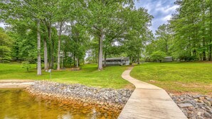 A pond with a concrete walkway, surrounded by trees and a house in the background. - Evergreen - Lakefront Home With Dock, Screened Porch, AC & Kayaks (Moneta)