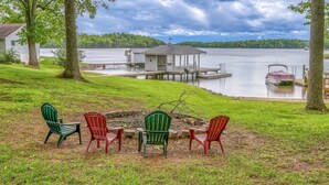 A lakeside property with a dock, a small cabin, and a fire pit with chairs. - Evergreen - Lakefront Home With Dock, Screened Porch, AC & Kayaks (Moneta)