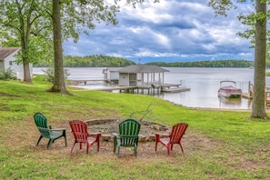 A lakeside property with a dock, a small cabin, and a fire pit with chairs. - Evergreen - Lakefront Home With Dock, Screened Porch, AC & Kayaks (Moneta)