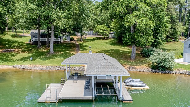 A floating dock with a covered seating area and a small building, surrounded by trees and a calm body of water. - Evergreen - Lakefront Home With Dock, Screened Porch, AC & Kayaks (Moneta)