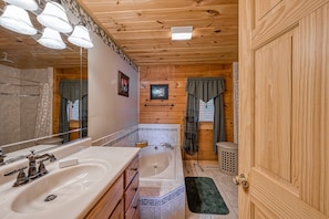 Une salle de bain rustique, avec une cabine en bois, un grand lavabo, une baignoire, un miroir et un rideau de douche.