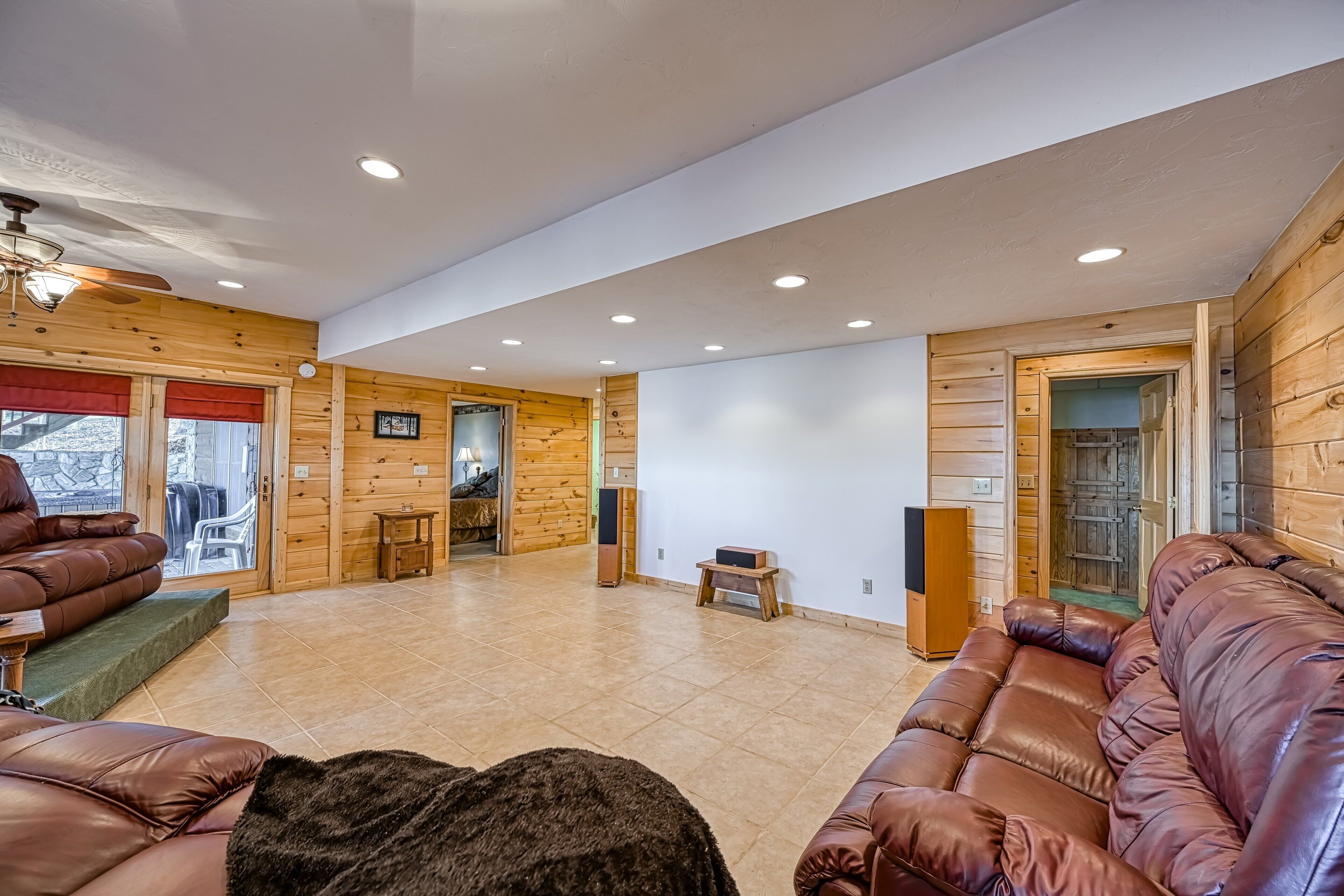 A spacious living area with wooden walls, a ceiling fan, and a fireplace.