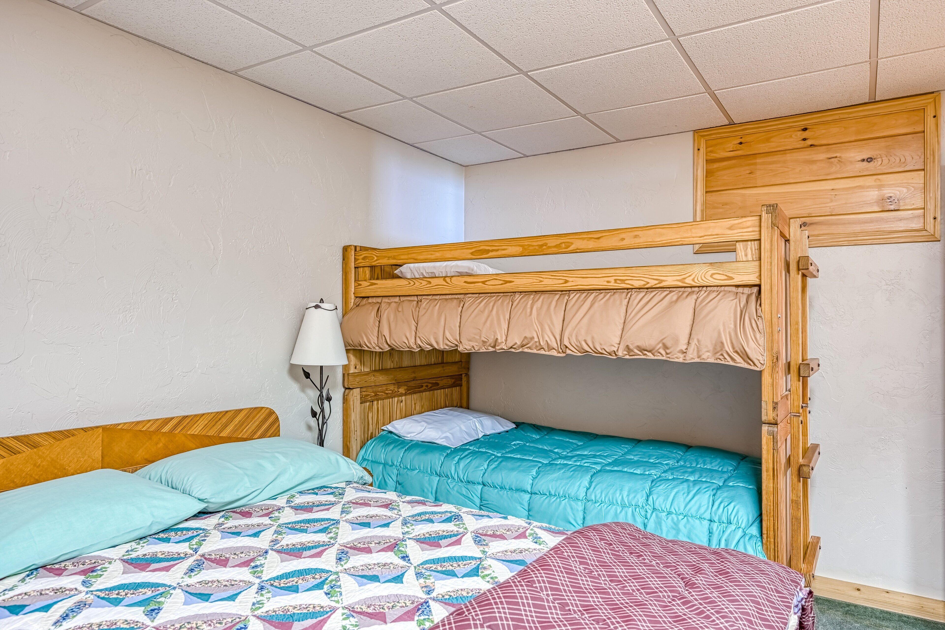 Une chambre avec un lit superposé, une tête de lit en bois, une lampe et une couvre-lit à motifs.