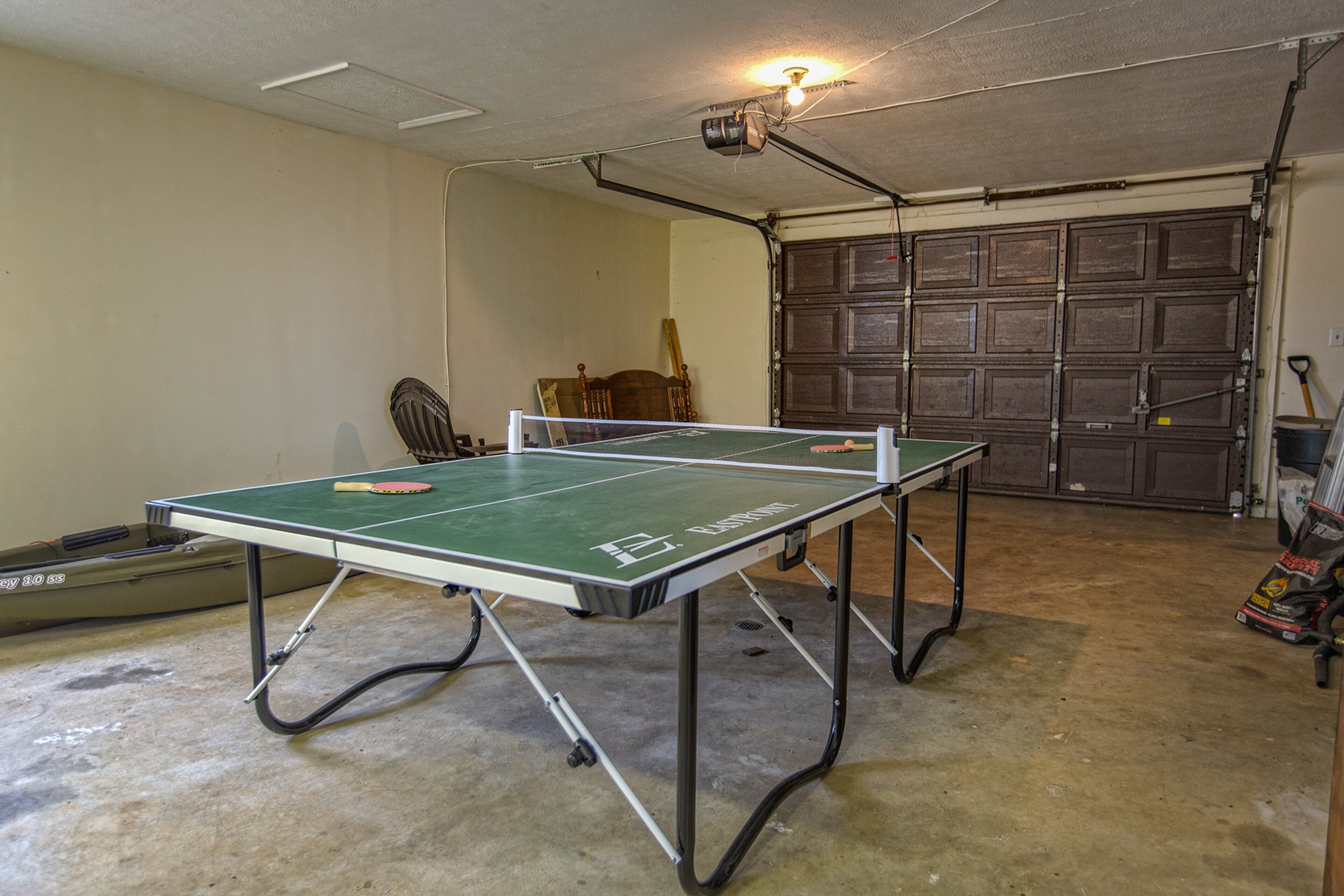 A ping pong table in a garage with a ceiling fan, a wooden chair, and a garage door in the background.