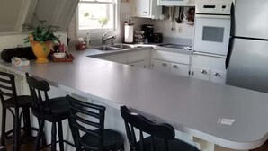 Keittiössä on valkoiset kaapit, keskellä sijaitseva saareke, jossa on baarituolit, jääkaappi ja mikroaaltouuni.