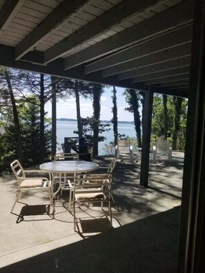A covered patio with a round table and chairs, overlooking a body of water and trees. - Cardinals Nest Smith Mountain Lake (Huddleston)