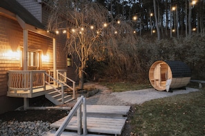 A wooden cabin with a deck, a sauna, and string lights. - Private Cabin in the Woods: Hot Tub, Pool, Sauna (Skaneateles)
