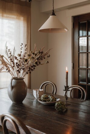A dining table with a vase of dried flowers, a candle, and artichokes. - Private Cabin in the Woods: Hot Tub, Pool, Sauna (Skaneateles)