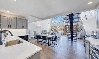 Una cocina moderna con armarios grises, encimera blanca y una zona de comedor con mesa y sillas.