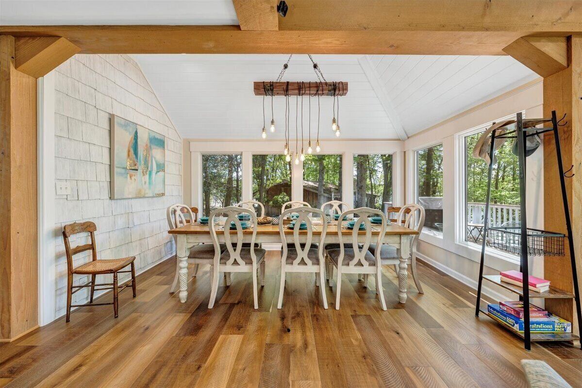 A dining area with a wooden table and chairs, a hanging light fixture, and a bookshelf.