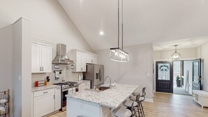 A modern kitchen with white cabinetry, a large island, stainless steel appliances, and bar stools. - Lawi Lakehouse - Stunning Lakefront Oasis With a Kayak, Large Deck, Games, & Tranquil Views (Wirtz)