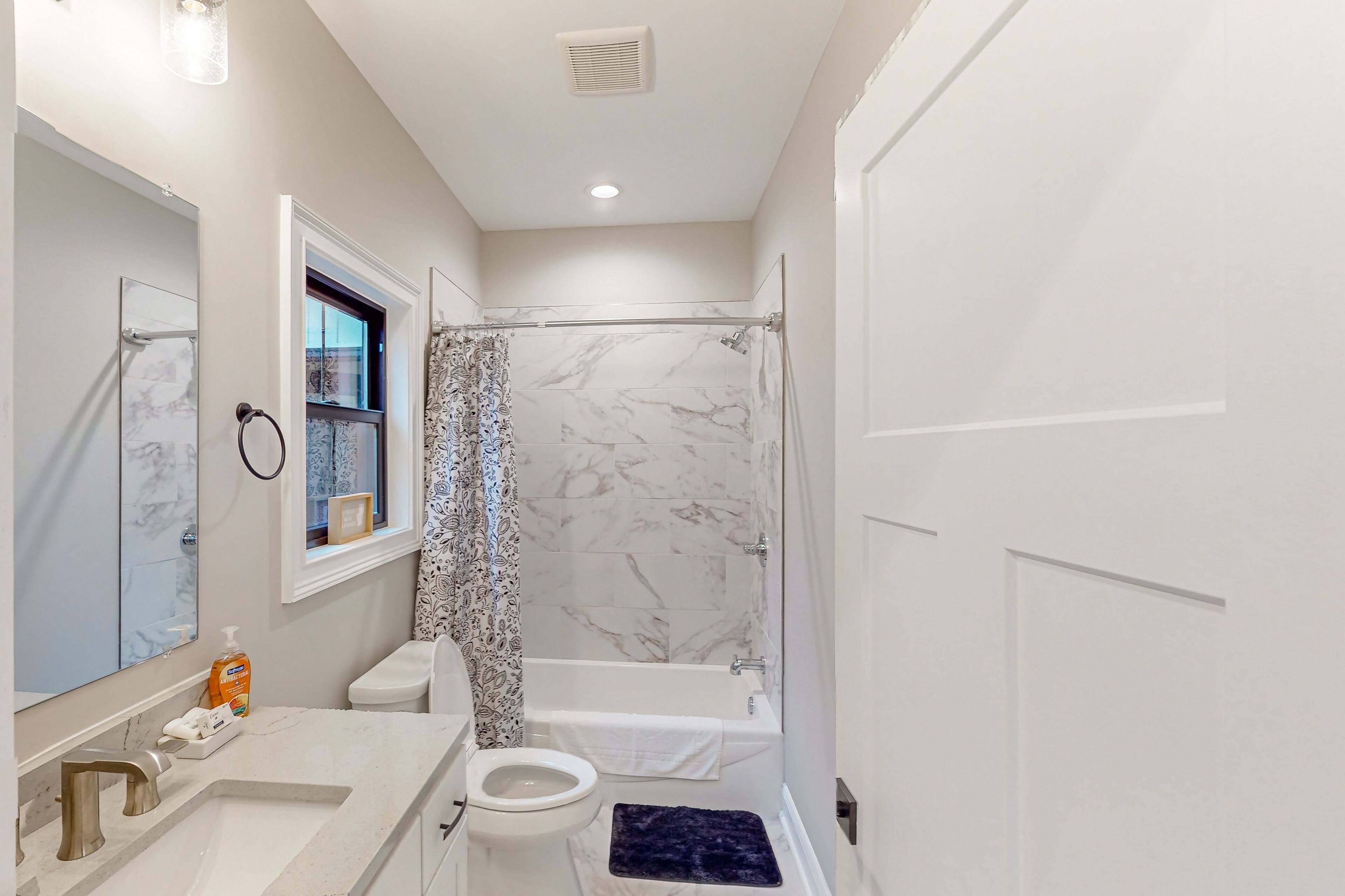 A bathroom with a marble shower, a white toilet, and a sink with a mirror.
