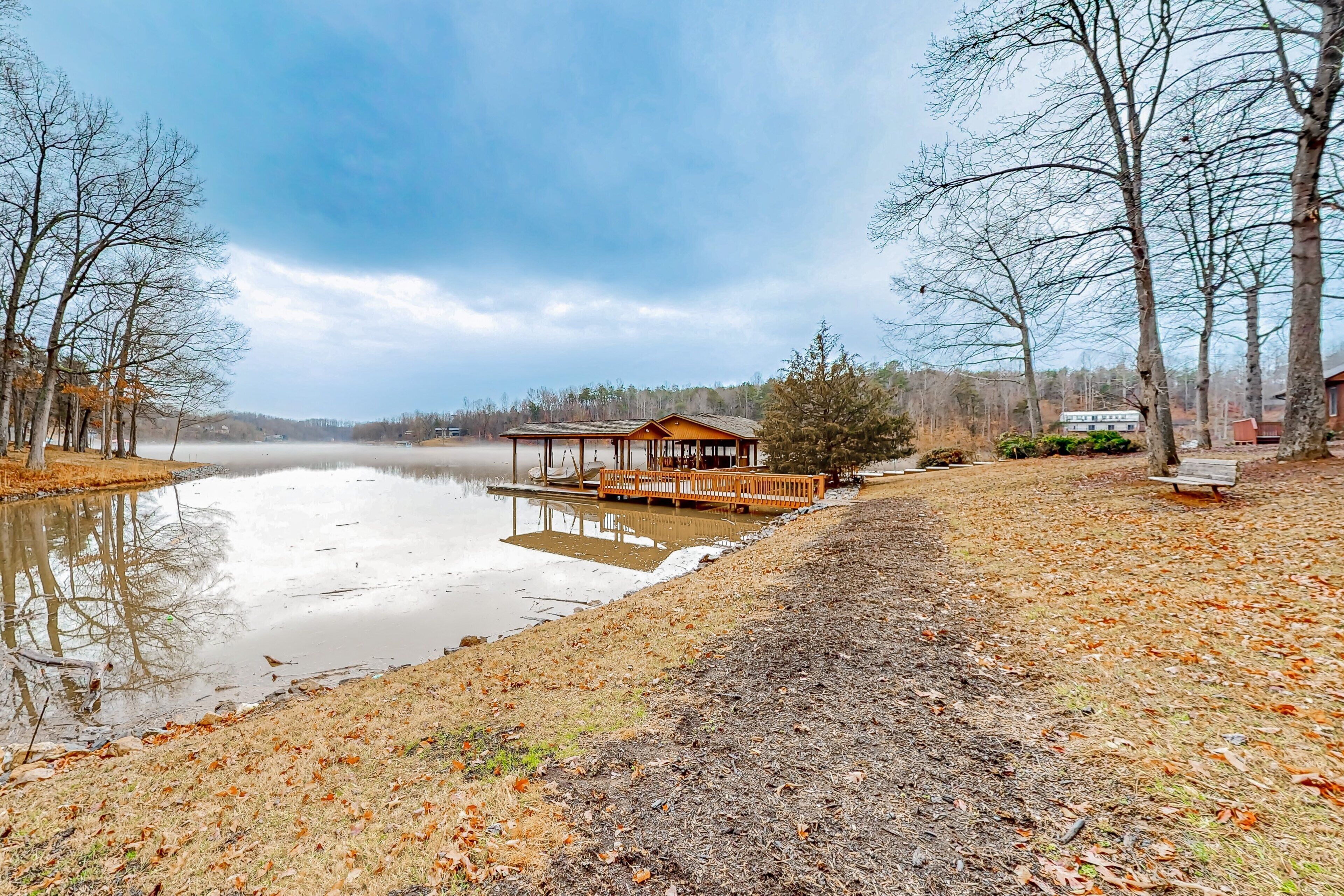 A lakeside cabin with a dock, surrounded by trees and a clear sky.