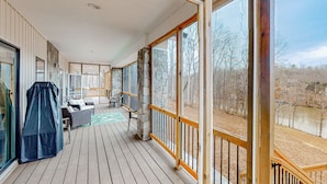 A covered deck with a dining area, stone pillar, and large windows. - Lawi Lakehouse - Stunning Lakefront Oasis With a Kayak, Large Deck, Games, & Tranquil Views (Wirtz)