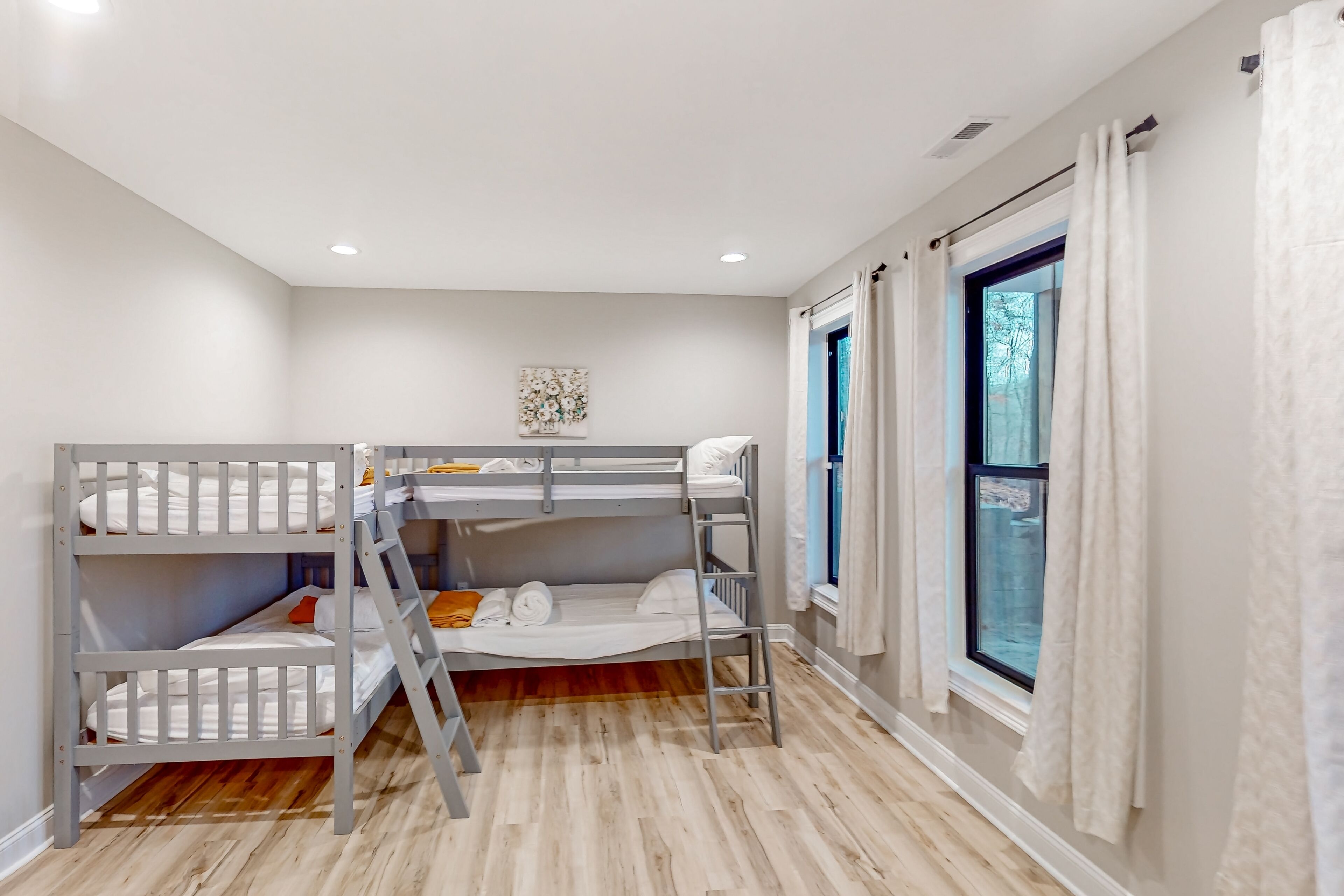 Una habitación con literas, una escalera, una ventana con cortinas y un cuadro en la pared.