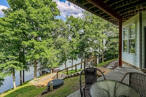 A covered outdoor area with a view of a lake, a wooden deck, and a glass table and chair. - Still Waters - Lakefront Luxury Home With Views, Dock, Home Theater & Game Room (Goodview)