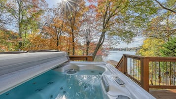 A hot tub on a wooden deck with a view of a lake and autumn trees.