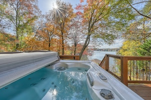 Un jacuzzi en una terraza de madera con vista a un lago y árboles otoñales.