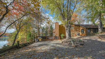 A stone cabin with a chimney, surrounded by trees and a gravel path.
