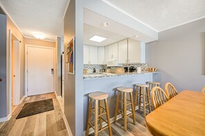 Eine moderne Küche mit weißen Schränken, einer Mikrowelle und einer gefliesten Spritzschutzwand. Es gibt Holzstühle und einen Holzessttisch.