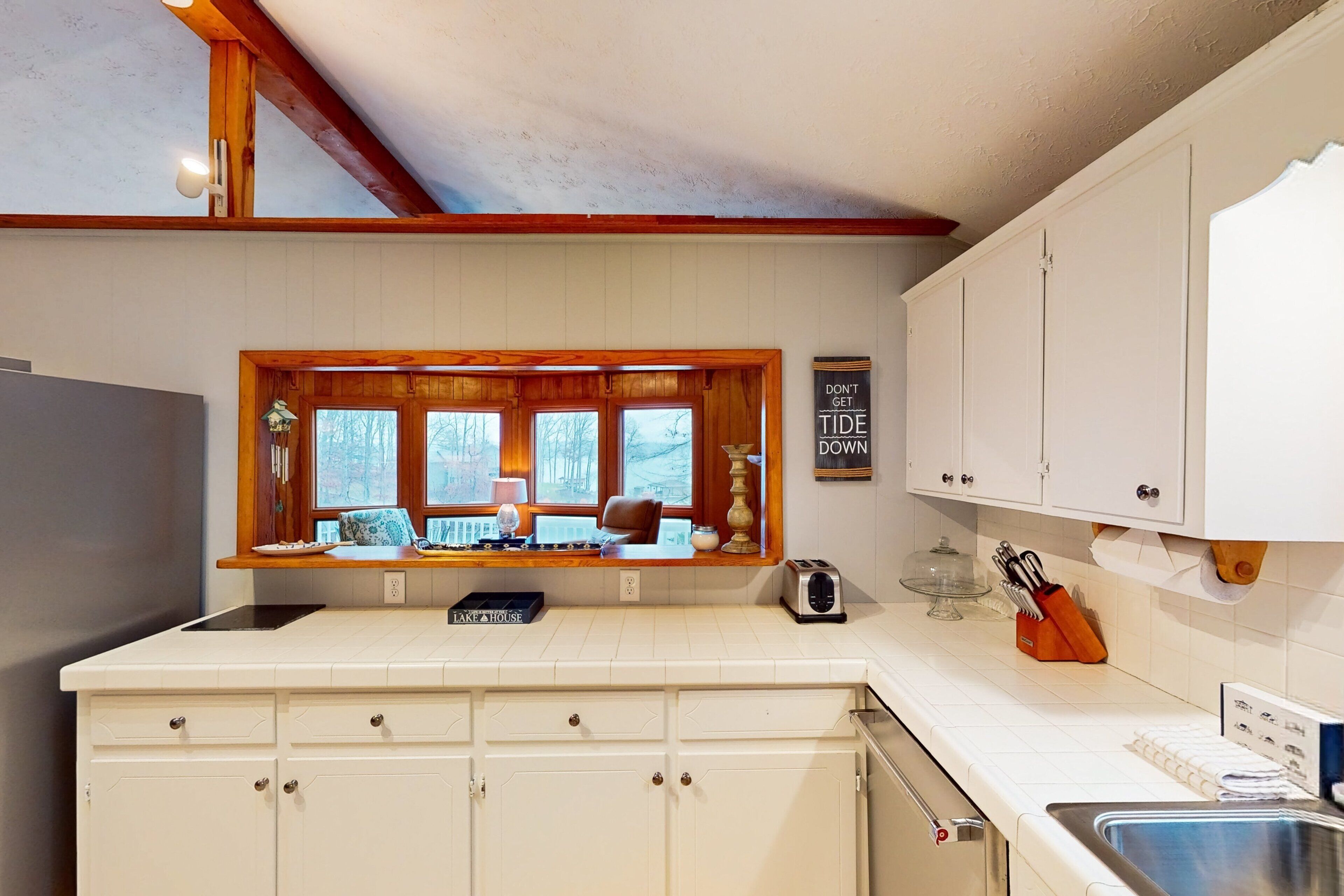 Una cocina con ventana, armarios blancos, un tostador y un lavamanos.