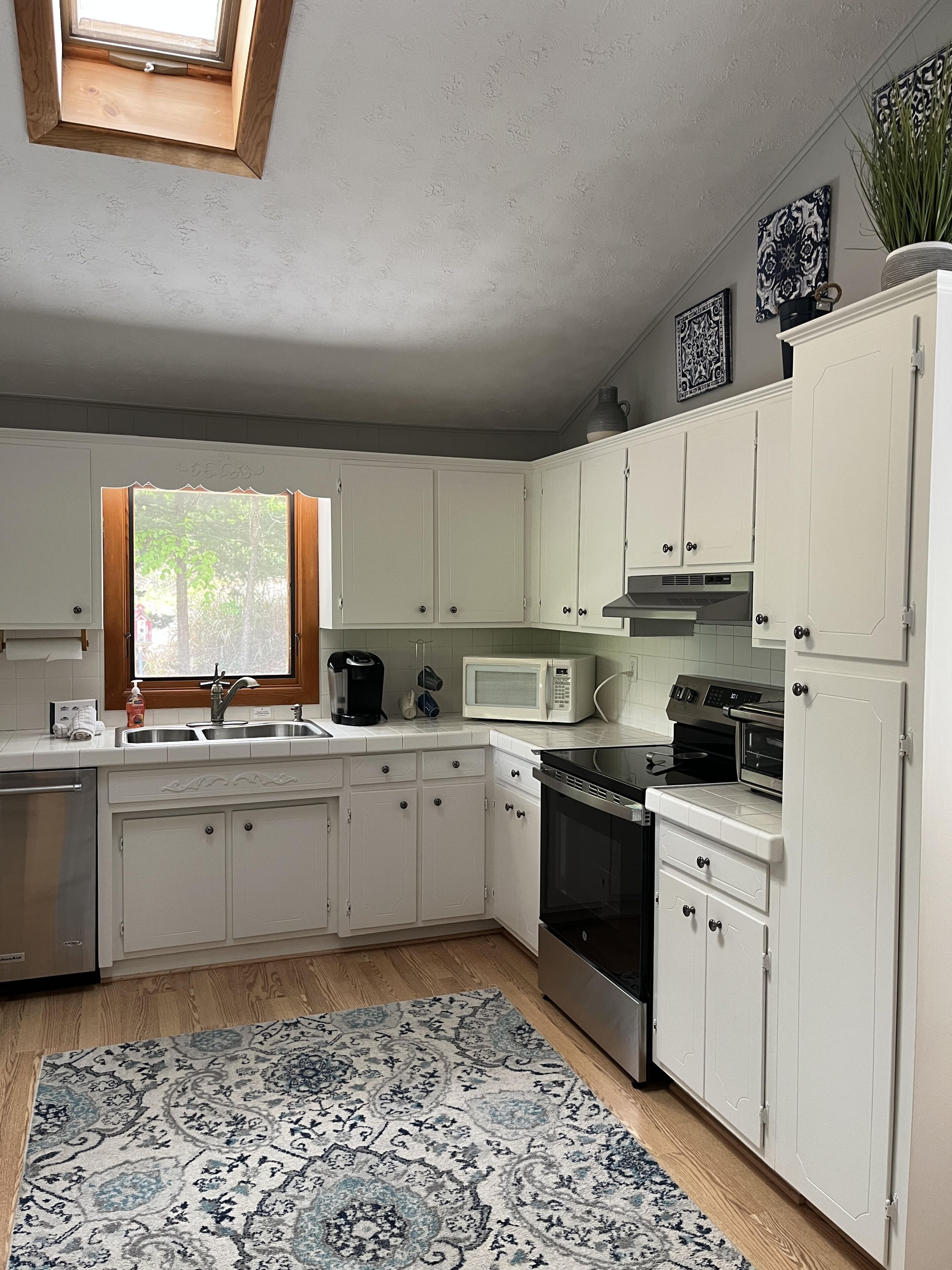 Una cucina con mobili bianchi, un forno a microonde, un forno e un lavello.