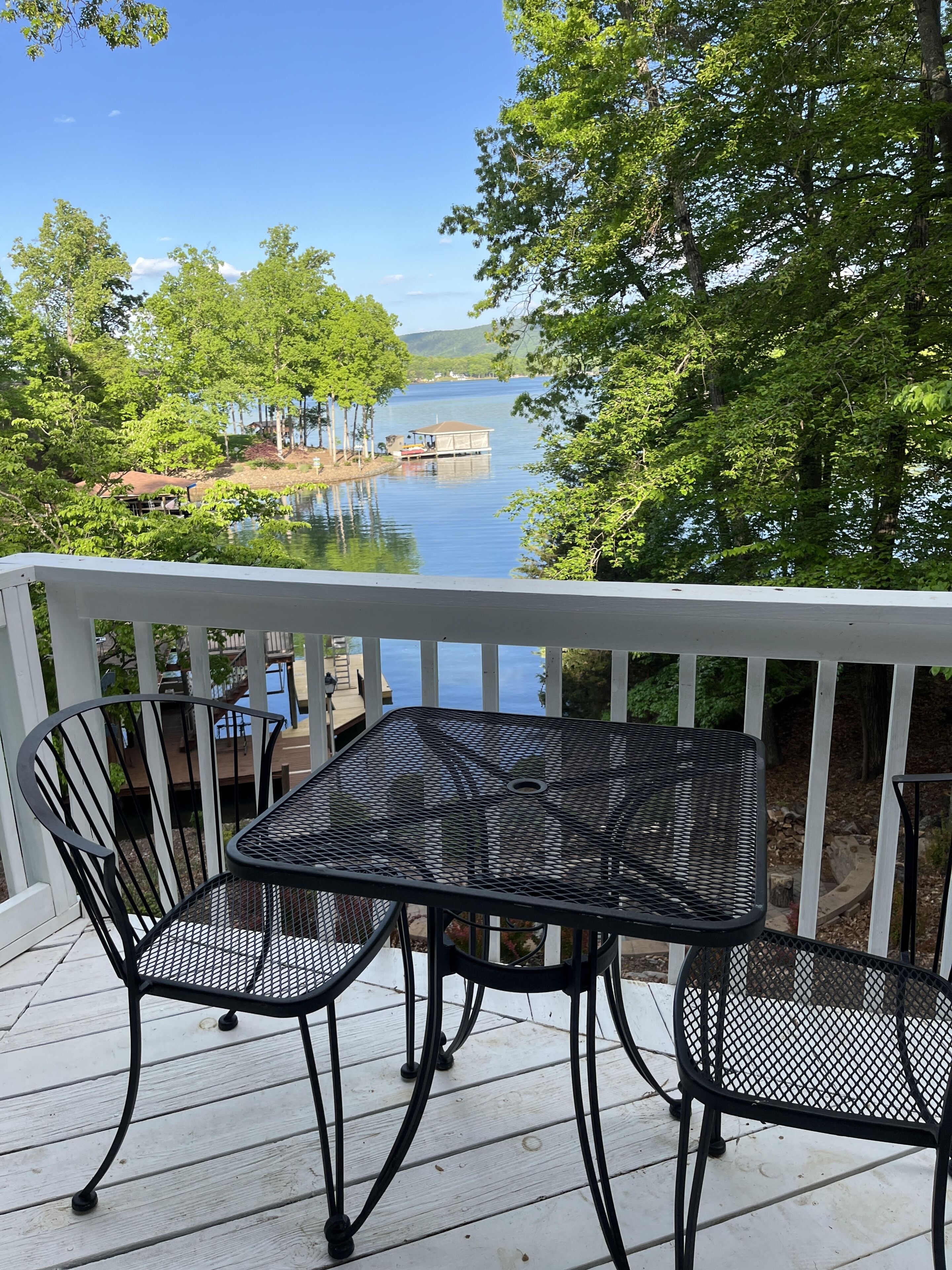 Eine Terrasse mit Tisch und Stühlen mit Blick auf einen See, umgeben von Bäumen.