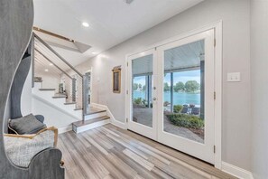 Een modern interieur met een trap, een zithoek en uitzicht op een wateroppervlak door glazen deuren.