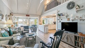 A spacious living area with a high ceiling, a television, and a bookshelf. - Cottage at the Lake - Waterfront Lake-view Home With Dock, Fireplace, Pool Table, Kayaks, & Firepit (Moneta)