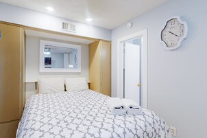 A hotel room with a bed, a mirror, a clock, and a door.