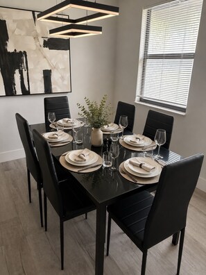 A dining room with a rectangular table set for four, black chairs, a vase with greenery, and a modern pendant light. - Port Charlotte Family Retreat with Pool & Hot Tub & 10 mins to the Beach (Port Charlotte)