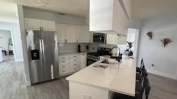 Cocina moderna con armarios blancos, refrigerador de acero inoxidable, microondas y estufa a gas.