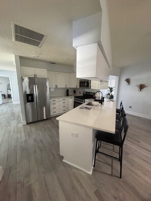 A modern kitchen with white cabinetry, a stainless steel refrigerator, a microwave, and a gas stove. - Port Charlotte Family Retreat with Pool & Hot Tub & 10 mins to the Beach (Port Charlotte)