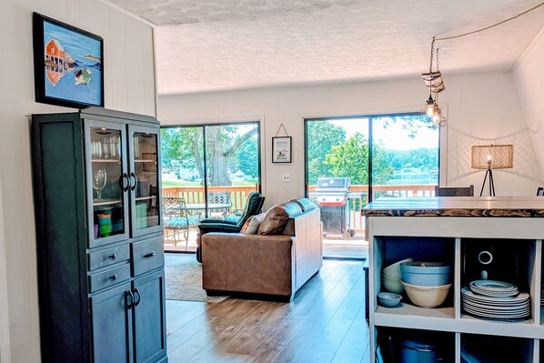 A spacious living area with a sofa, dining table, and a cabinet with glass doors. - Dock Sun Point - Lakefront Home for Easy Boating, Fishing, Private Dock & Ac/wifi, Dogs ok! (Huddleston)