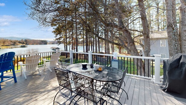 A deck with a table and chairs overlooking a lake, surrounded by trees and a white fence. - Sail Away - Waterfront Home With Private Beach on the Lake, hot Tub, & Dock (Huddleston)