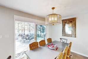 Un comedor con una mesa, sillas de mimbre, una lámpara colgante y un amplio ventanal con vistas a muebles de exterior.