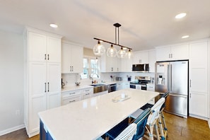 A modern kitchen with white cabinets, a large island, stainless steel appliances, and a hanging light fixture. - Sail Away - Waterfront Home With Private Beach on the Lake, hot Tub, & Dock (Huddleston)